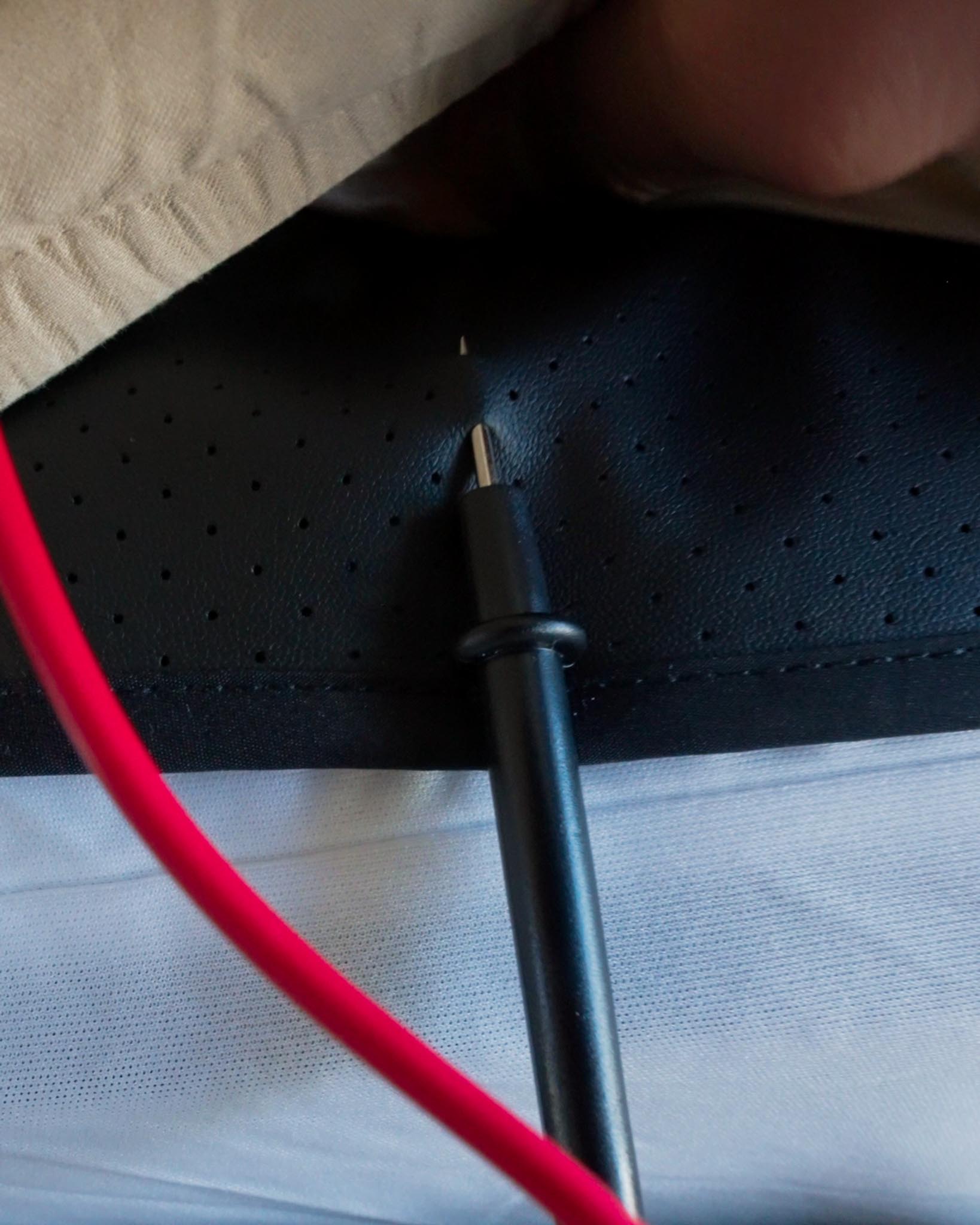 Close-up of multimeter probe touching Earthbound grounding mat under bed sheet to test conductivity