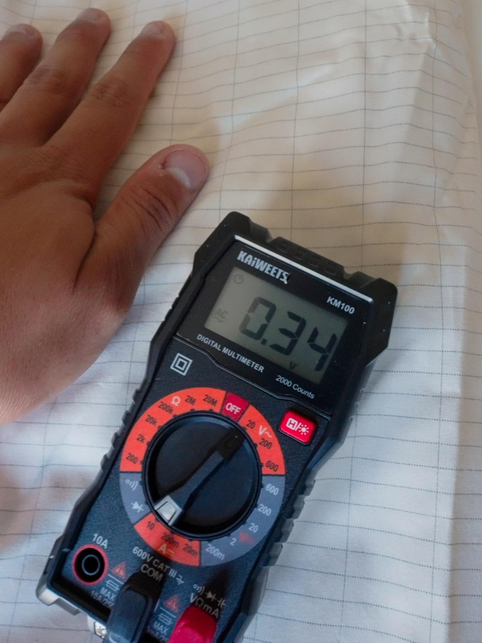 Hand resting on grounding sheet showing 0.34V reading on digital multimeter