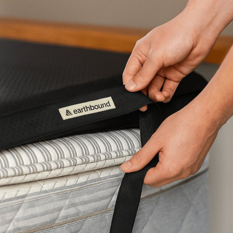 Person securing a black strap on a folded mattress with 'earthbound' branding.