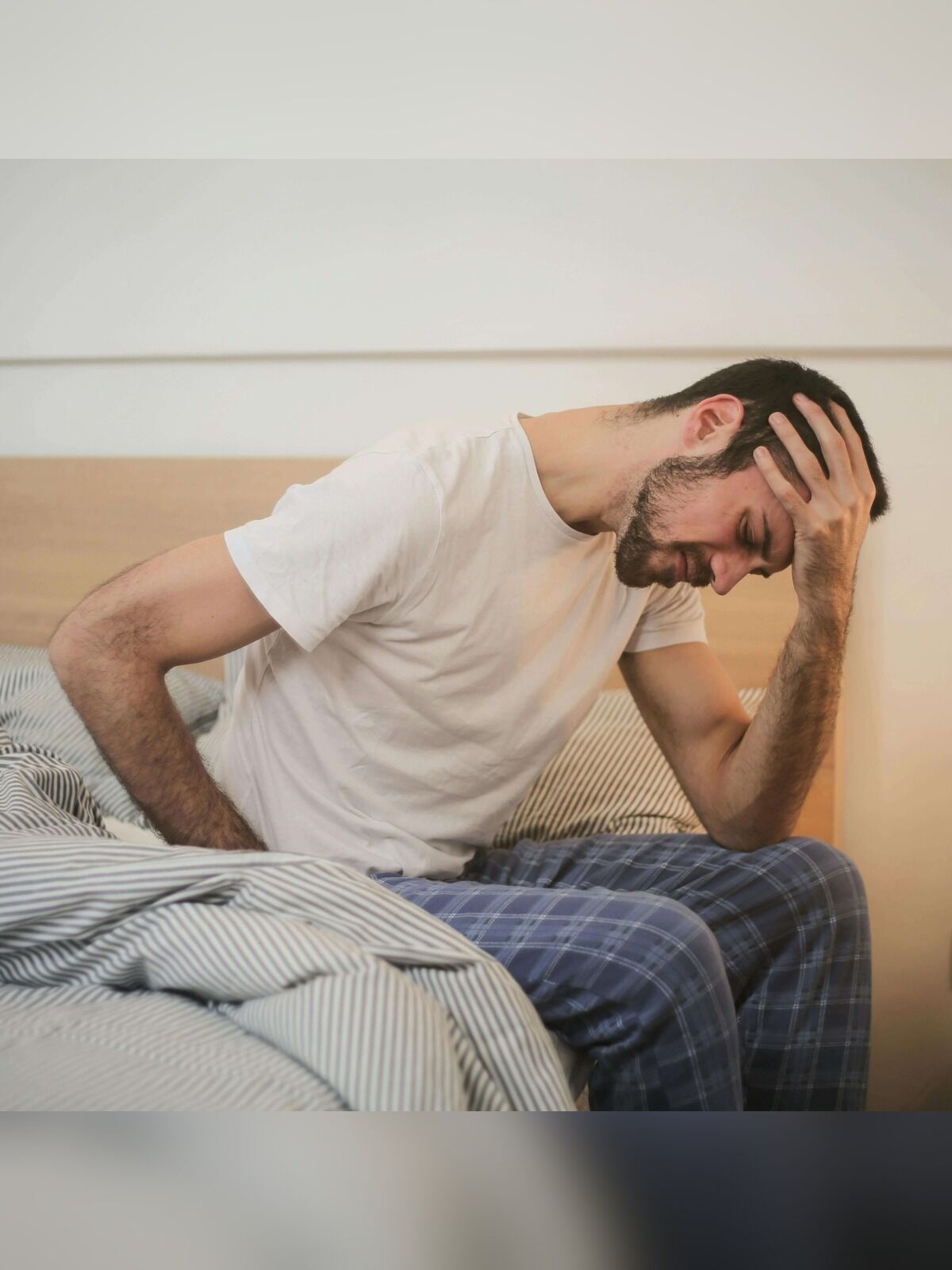 Man sitting on a bed with a distressed expression, holding his head.