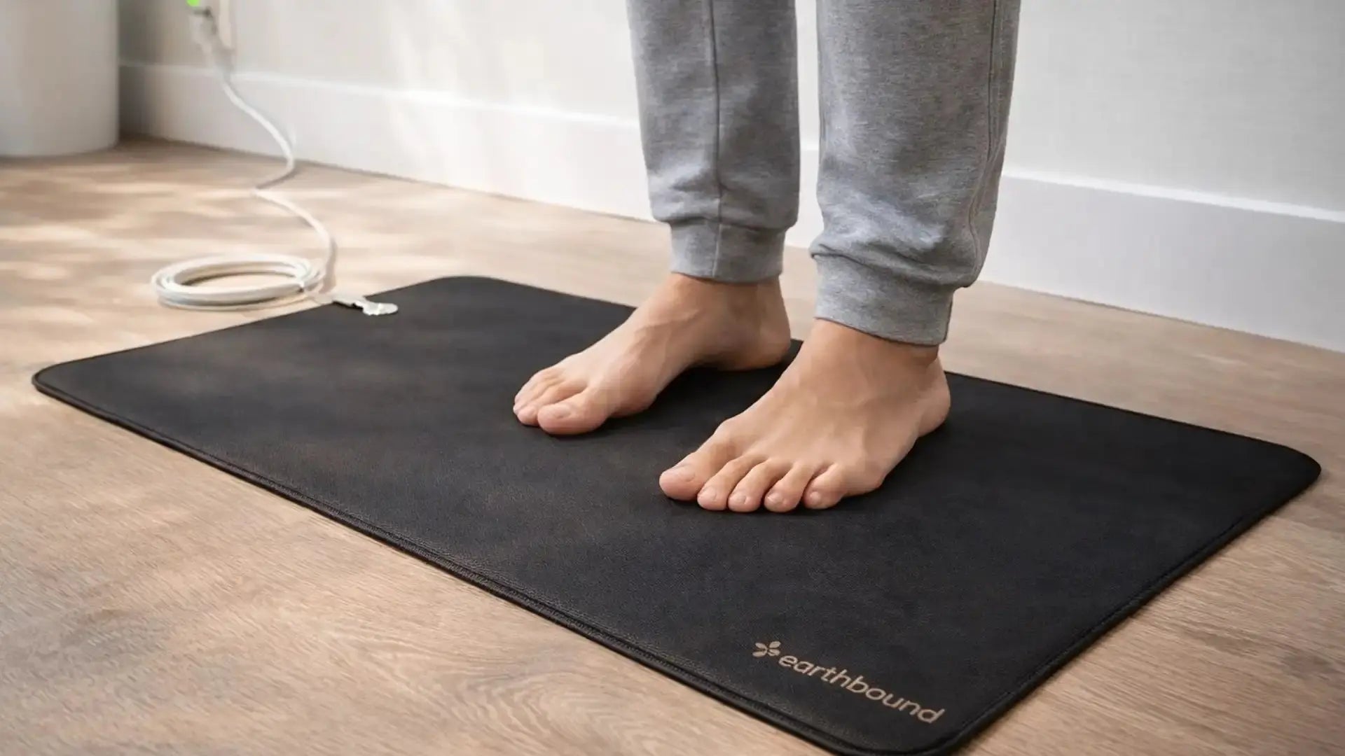 Person standing barefoot on a premium grounding mat connected to a wall outlet in a home setting