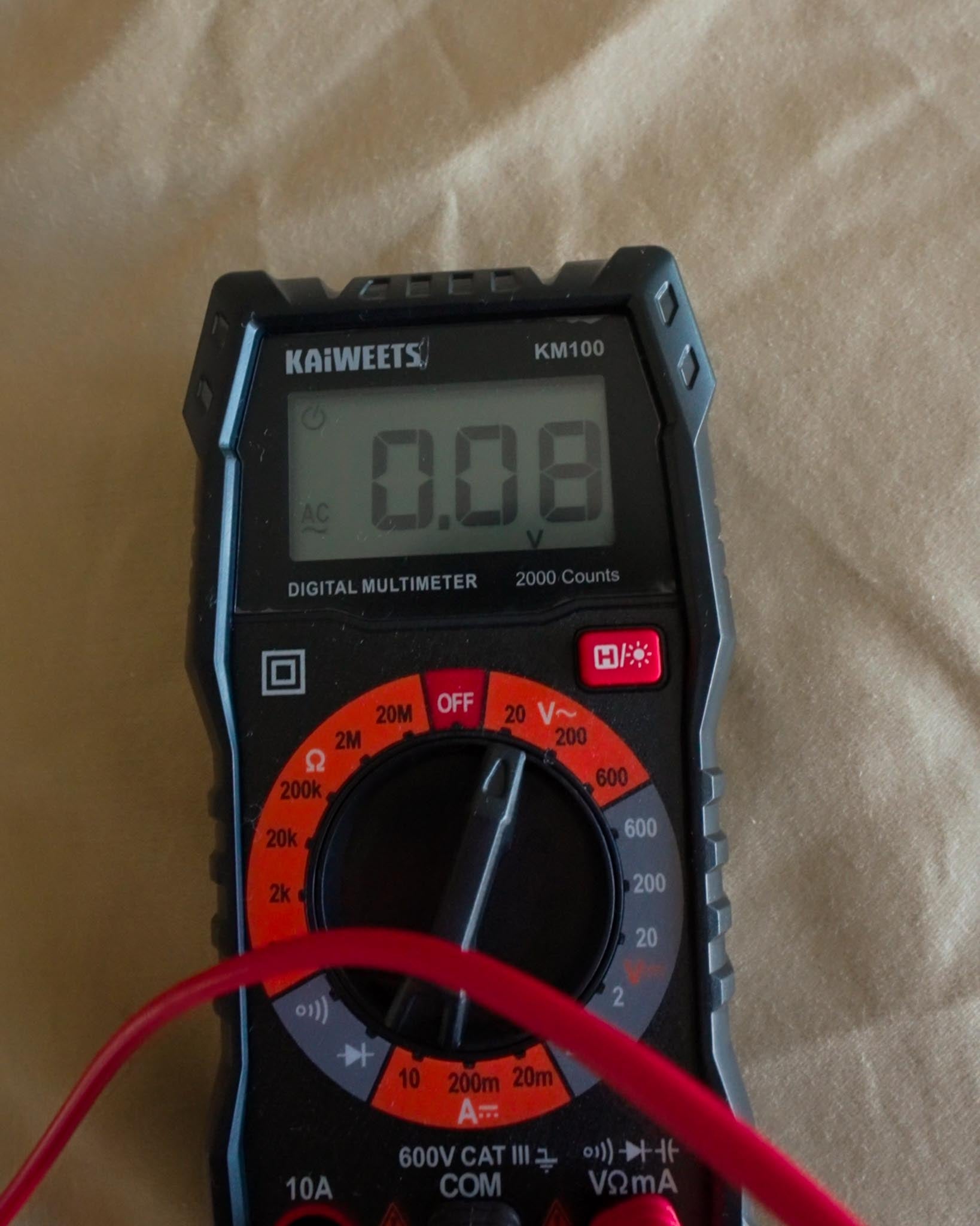 Digital multimeter displaying near-zero AC voltage reading on grounded bed sheet