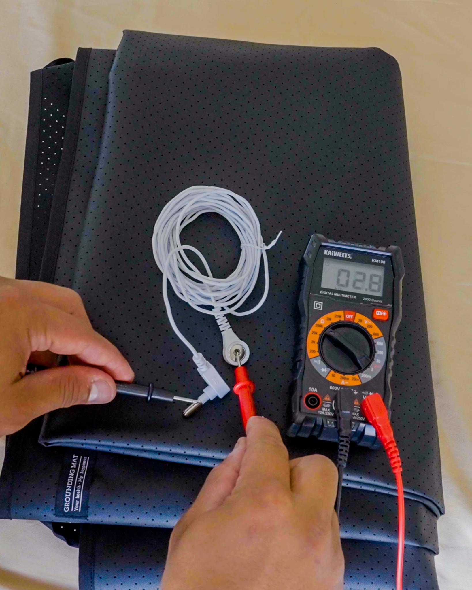 Measuring grounding cord connection on grounding mat with digital multimeter showing 0.28V reading