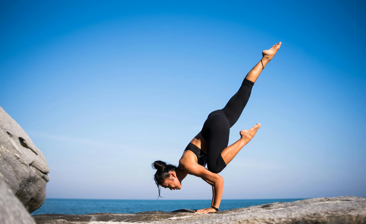 Woman doing yoga handstand by beach