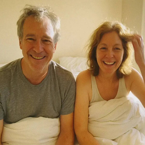 Man and woman sitting on a bed in a bright room